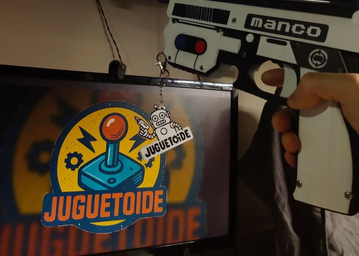 Un colgante con el robot de Juguetoide enganchado en una MANCO, delante de una pantalla con el logo de Juguetoide.