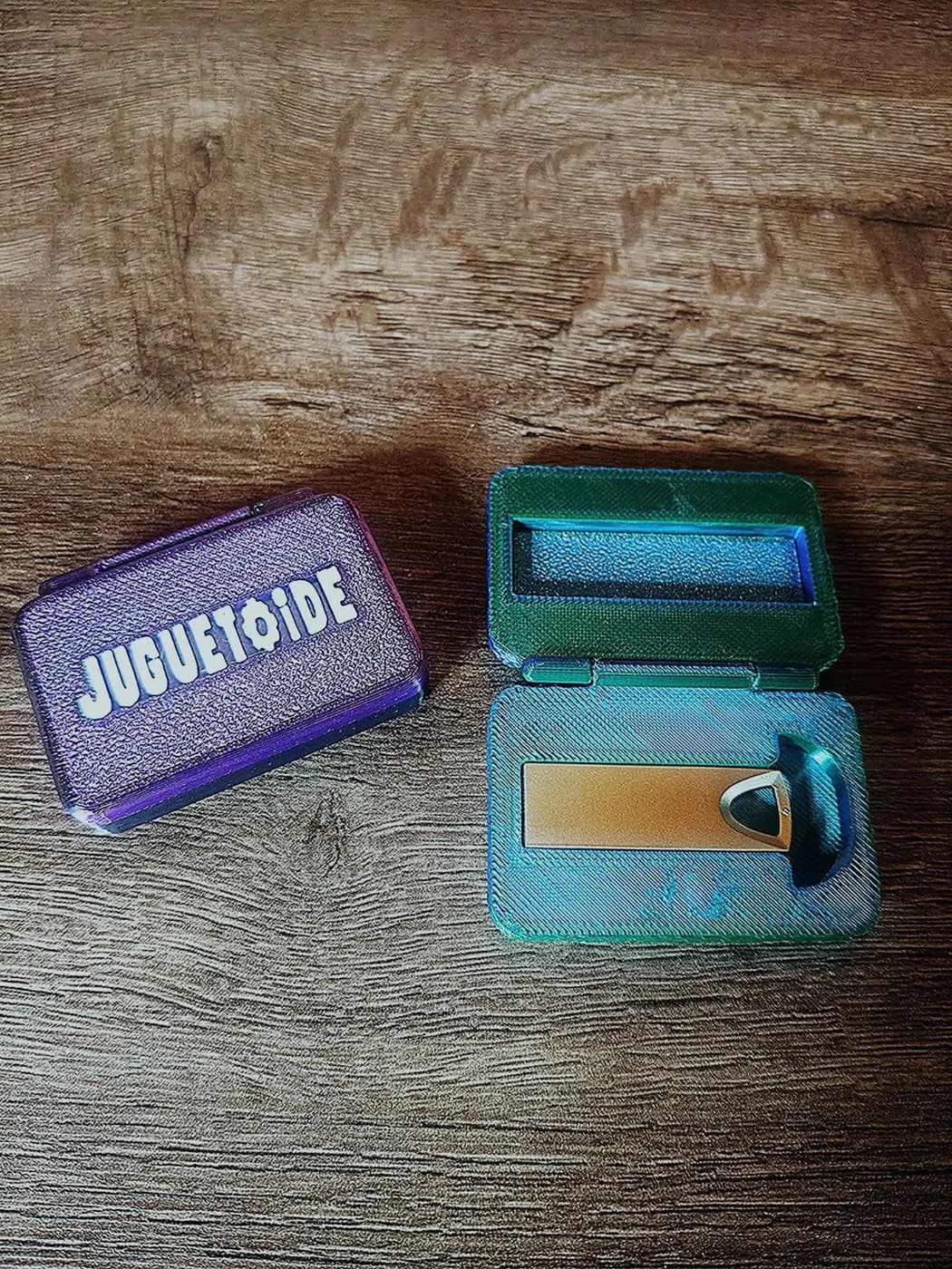 Dos estuches con el logo de Juguetoide: uno violeta cerrado y uno verde abierto, con el pendrive adentro.