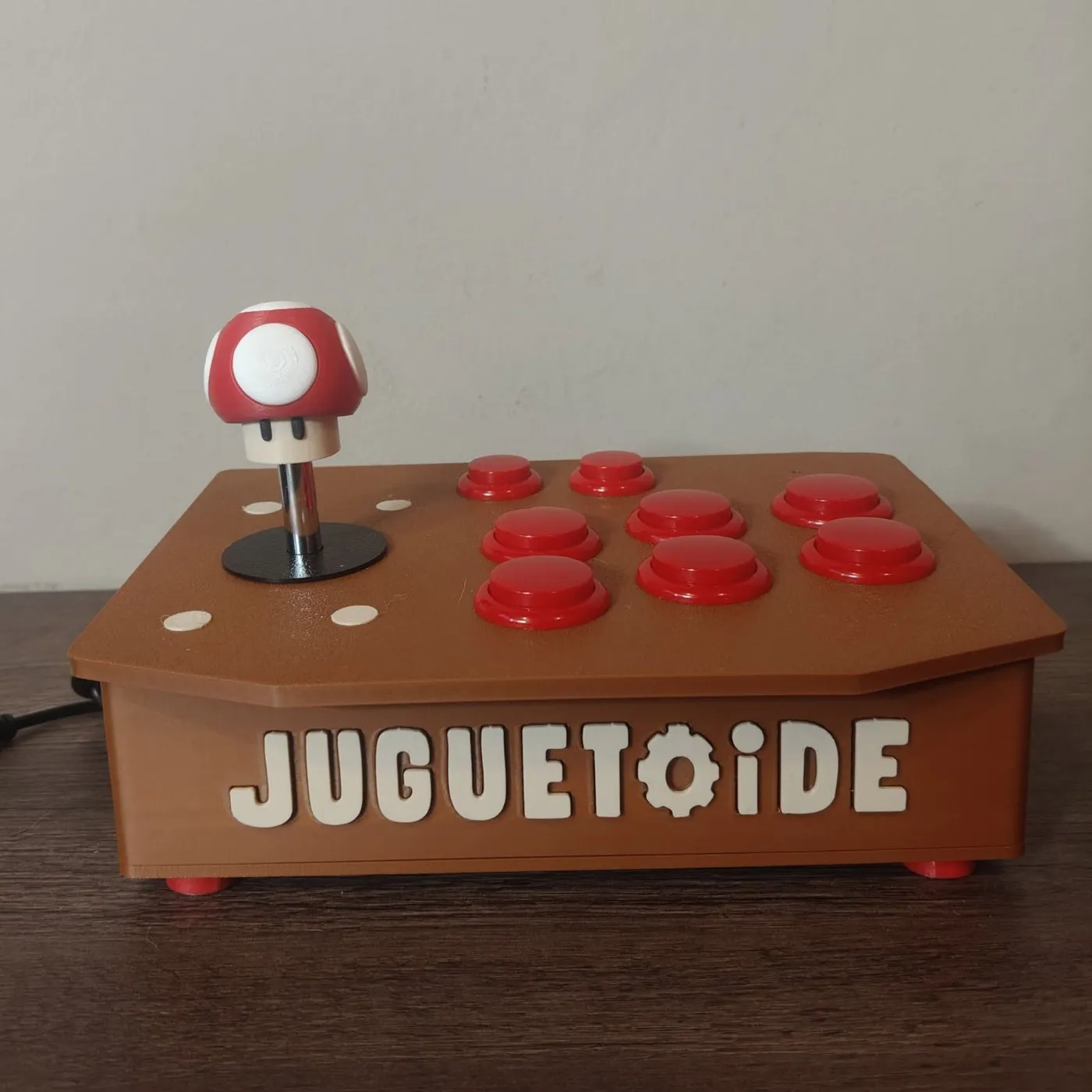 Un Juguetoide Stick marrón con botones rojos y la bocha con forma de hongo rojo.